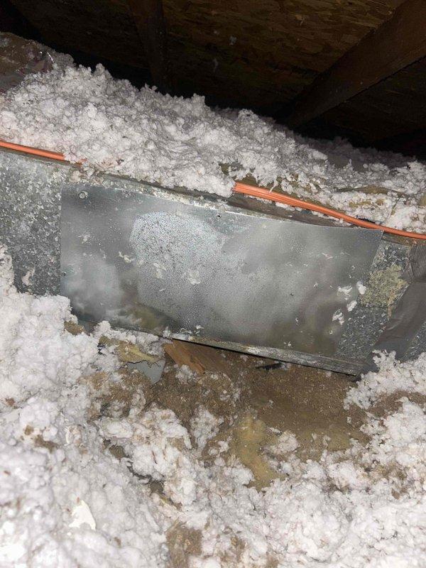 Responded to ceiling leak complaint suspected to be related to AC system. Accessed attic space and inspected HVAC ductwork and condensate drainage system. Found visible moisture condensation and discoloration on metal plenum box with water staining on surrounding surfaces. Inspected PVC condensate drain line with elbow joint near ductwork and confirmed proper drainage pathway. Documented conditions of post-flood AC unit showing signs of age and moisture exposure on metal components. Verified heating and cooling system remains operational at time of inspection.