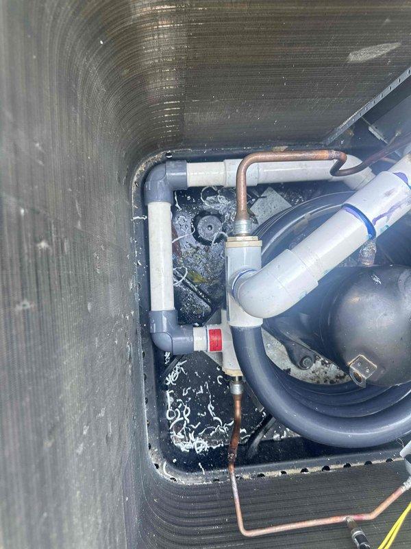 Performed warranty inspection on HVAC system air handler unit. Documented interior cabinet condition, noting standing water accumulation in drain pan with visible debris and sediment. Inspected refrigerant lines (copper and insulated), PVC condensate drainage piping, and condensate trap assembly for proper configuration and function. Photographed mechanical components within protective housing to document system status and drainage concerns for warranty evaluation.