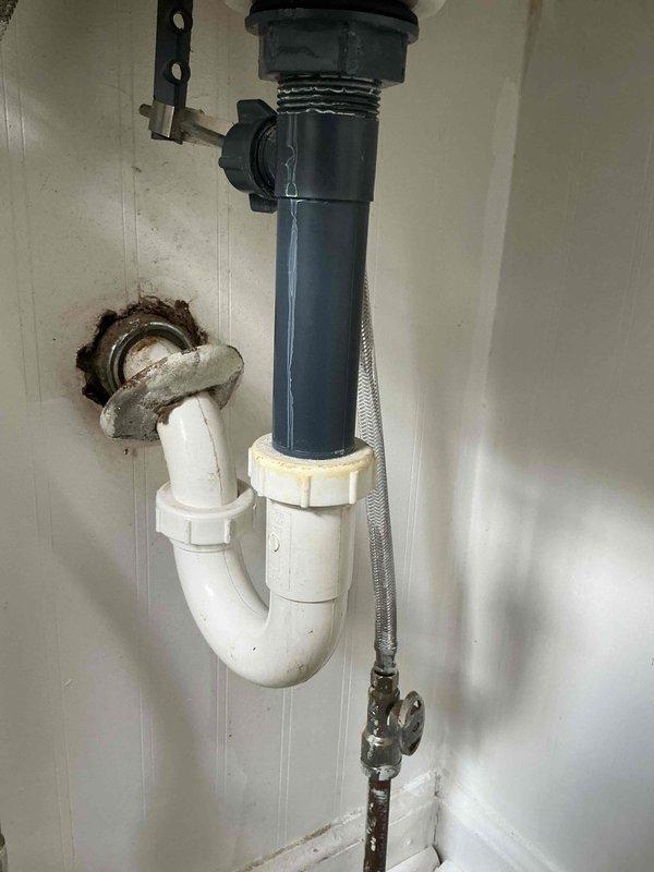 Responded to water leak complaint under bathroom vanity. Upon inspection, identified active moisture intrusion with visible water damage and rust-colored staining on cabinet interior surfaces and beadboard wall. Examined drain assembly, P-trap configuration, and supply line connections. Found compromised seal at drain body connection and deteriorated P-trap gasket allowing water seepage. Documented existing water damage patterns indicating prolonged leak condition affecting vanity cabinet and adjacent wall cavity behind laundry area. Tightened all drain connections, verified proper P-trap alignment, and inspected braided supply lines and shutoff valves for integrity. Recommended monitoring for additional leakage and potential cabinet replacement due to extent of water damage observed.