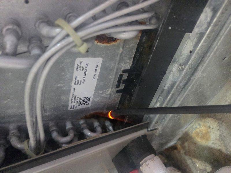 Responded to customer complaint of AC system running but not cooling adequately throughout residence. Upon inspection, discovered critical electrical fault with evidence of active arcing and overheating on wiring within air handler cabinet. Glowing orange-red spot observed on electrical conductor indicating dangerous heat buildup and potential fire hazard. System showed signs of age with rust accumulation and general wear on cabinet components. Documented equipment condition with photographic evidence of electrical failure and deteriorated internal components. Immediate shutdown of system recommended due to safety concerns until proper electrical repairs can be completed to resolve arcing issue and restore safe operation.