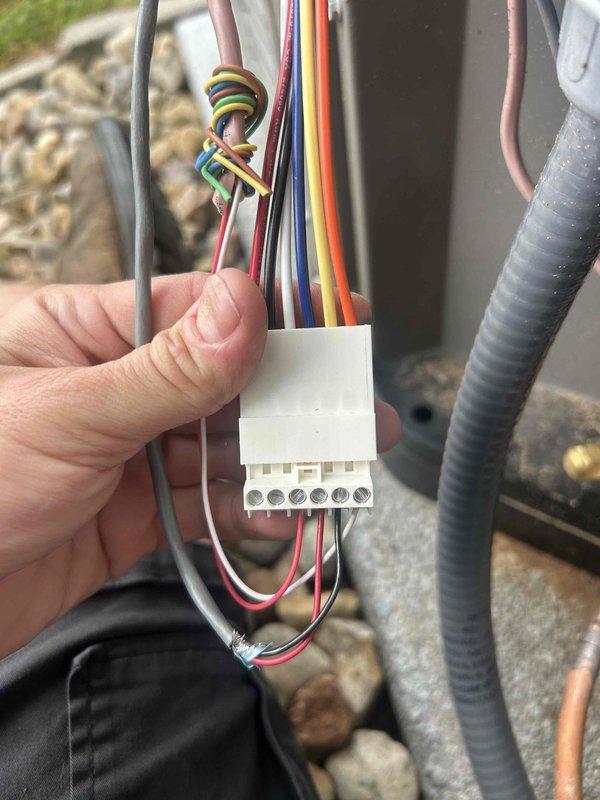 Responded to callback regarding newly installed split system air conditioner experiencing intermittent communication loss between outdoor condensing unit and indoor air handler, resulting in unexpected system shutdowns. Inspected electrical connections at outdoor unit and indoor furnace, examining terminal block wiring harness with multiple low-voltage control wires and verifying proper connections between thermostat, condenser, and air handler. Troubleshot communication wiring between components, checked refrigerant line set installation, and documented existing wiring configuration for warranty follow-up on two-week-old installation.