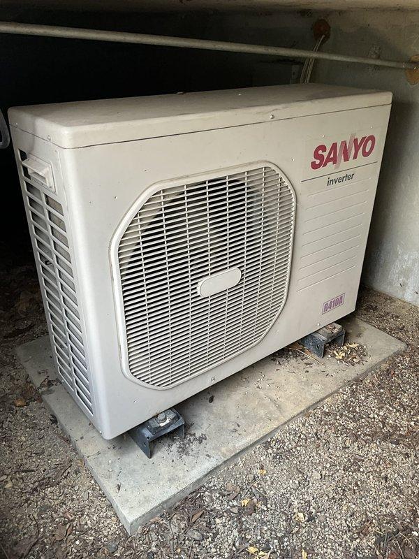 Conducted technical assessment of existing mini-split system at commercial café location. Documented current equipment configuration including outdoor Sanyo inverter-driven condenser unit utilizing R410A refrigerant and indoor floor-mounted air handler with protective grille assembly. Photographed both components to capture existing conditions, noting outdoor unit placement on concrete pad with visible weathering and indoor unit integration within floor framing between wooden structural members. Coordinated site access with on-site management to complete turnover inspection and equipment evaluation for estimate preparation.