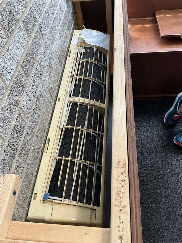 Conducted technical assessment of existing mini-split system at commercial café location. Documented current equipment configuration including outdoor Sanyo inverter-driven condenser unit utilizing R410A refrigerant and indoor floor-mounted air handler with protective grille assembly. Photographed both components to capture existing conditions, noting outdoor unit placement on concrete pad with visible weathering and indoor unit integration within floor framing between wooden structural members. Coordinated site access with on-site management to complete turnover inspection and equipment evaluation for estimate preparation.