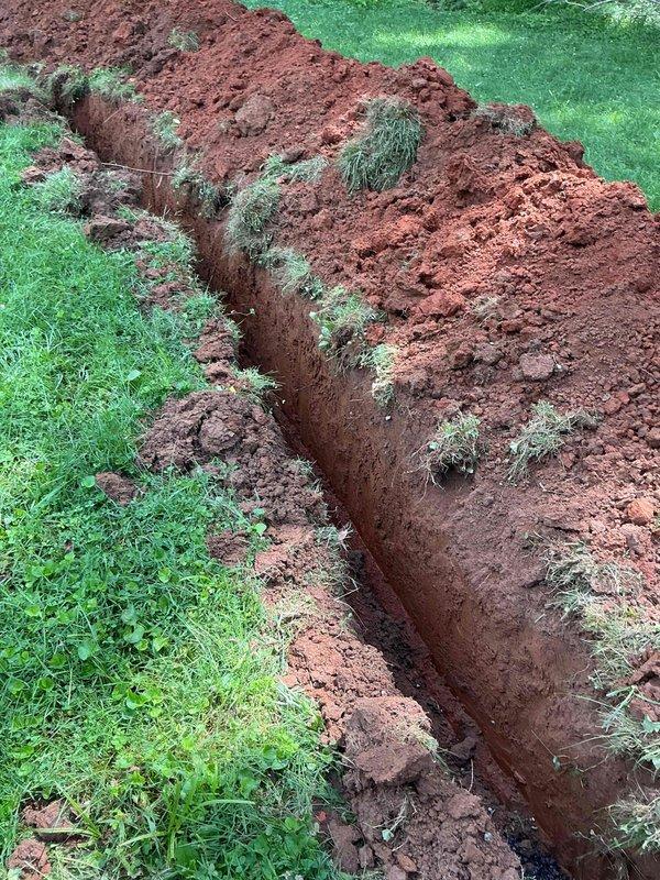 Excavated residential lawn to access and replace damaged water supply line. Trenched approximately 1-2 feet wide and several feet deep through clay-rich soil to expose existing white pipe. Removed old water line and installed new orange pipe sections, ensuring proper alignment and connection. Backfilled trench with excavated soil and prepared site for final restoration. All work completed using mini excavator equipment with minimal disruption to surrounding lawn areas.