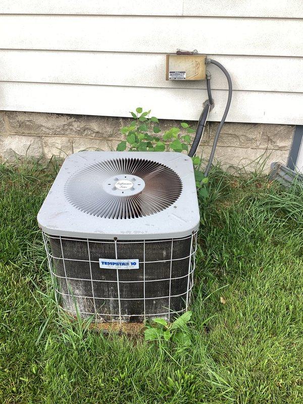 # HVAC Service Call - No Cooling Condition

Responded to service call for no cooling on 10+ year old Tempstar residential air conditioning system. Upon arrival, found thermostat displaying 79°F with no cooling occurring. Performed visual inspection of outdoor condenser unit, which showed significant age-related wear, dirt accumulation, and vegetation growth around base affecting airflow. Unit exhibited weathering consistent with extended outdoor exposure and lack of regular maintenance.

Conducted diagnostic evaluation of system components including electrical connections at exterior junction box, compressor operation, and refrigerant levels. Assessed condenser coil condition through protective wire mesh cage, noting debris buildup restricting heat transfer efficiency. Evaluated fan motor operation and blade condition at top grille assembly.

Cleared vegetation and debris from around condenser unit perimeter to restore proper airflow clearance. Inspected Honeywell digital thermostat fo