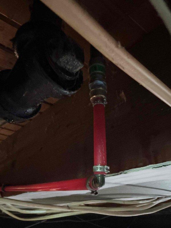Responded to reported slow drip on recently installed PEX water line in basement. Located leak at upper pipe connection point near ceiling joists. Tightened hose clamps securing pipe fittings and inspected full vertical run of red PEX tubing where it passes through floor structure. Verified proper mounting and support using existing metal clamp brackets. Confirmed leak resolution and checked surrounding connections for any additional moisture or potential failure points. System tested and operating properly with no further dripping observed.