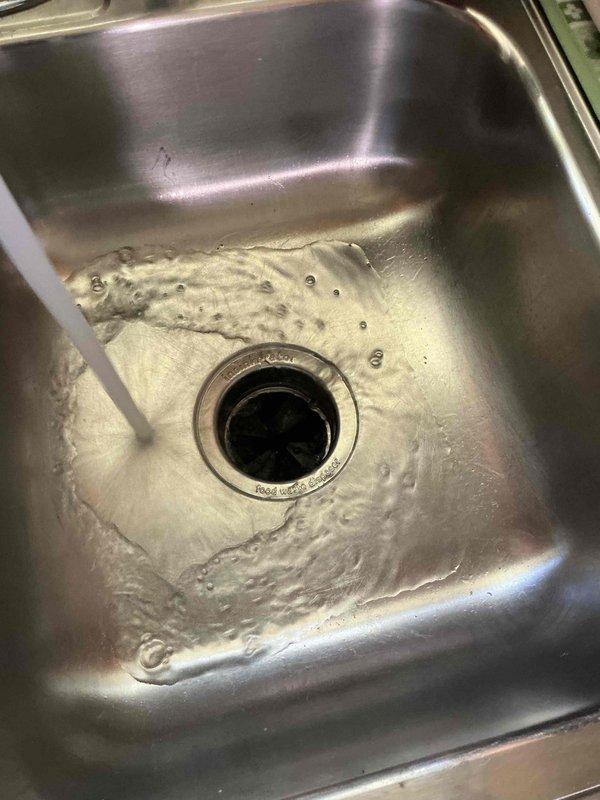 Responded to service call for non-operational and leaking garbage disposal unit that was over 20 years old. Upon inspection, found existing disposal unit showing signs of age-related deterioration with active leak present beneath sink cabinet. Placed catch bucket under unit to contain water discharge during assessment. Evaluated disposal condition, drainage connections, and mounting assembly. Due to the advanced age of the unit and combination of mechanical failure with active leaking, recommended replacement as most cost-effective solution. Documented existing installation configuration including PVC drain line connections and electrical supply for replacement specifications.