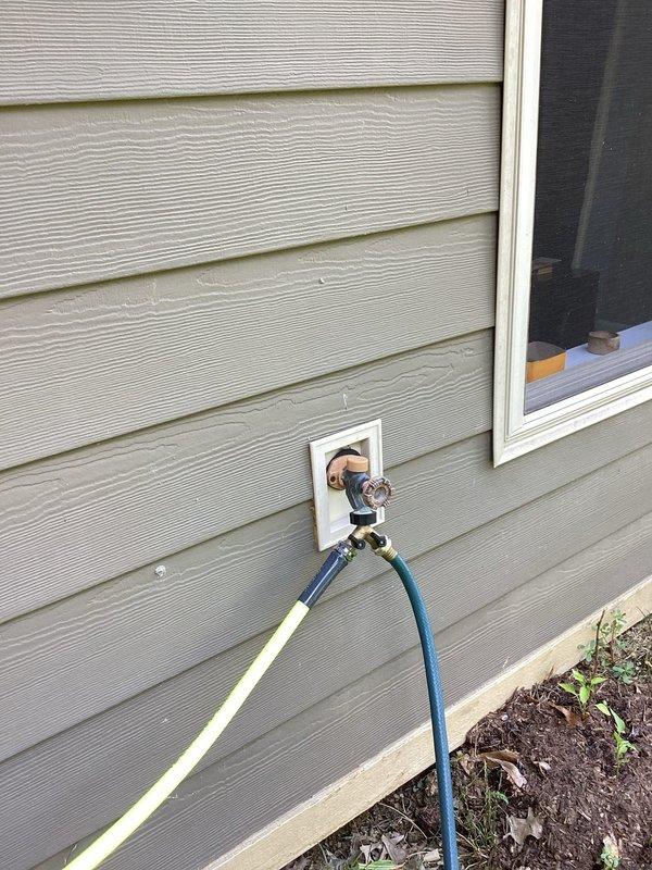 Responded to water leak complaint at exterior hose bib causing water intrusion into basement bedroom. Upon inspection, identified leaking outdoor spigot with dual hose Y-connector attachment on exterior wall above walkout basement. Diagnosed failed internal washer or valve seat allowing water to bypass the fixture and penetrate through wall penetration into interior living space. Recommended spigot replacement or repair to eliminate leak and prevent further water damage to basement bedroom.