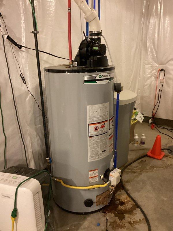 Completed monthly recurring plumbing inspection of residential water heater system. Upon examination, observed significant water staining and discoloration on concrete floor surrounding base of A.O. Smith water heater unit, indicating active or recent leakage. Documented current condition of installation including yellow flexible gas line connection, venting assembly with black motor/pump component, and surrounding utility room setup with protective plastic sheeting in place. Photographed water heater from multiple angles to capture extent of floor staining, unit specifications, safety labels, and connected plumbing infrastructure including colored supply pipes and electrical components. Provided water heater replacement estimates as requested for consideration due to observed leakage concerns and unit condition.