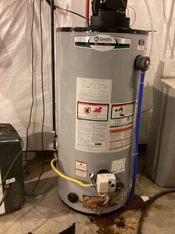 Completed monthly recurring plumbing inspection of residential water heater system. Upon examination, observed significant water staining and discoloration on concrete floor surrounding base of A.O. Smith water heater unit, indicating active or recent leakage. Documented current condition of installation including yellow flexible gas line connection, venting assembly with black motor/pump component, and surrounding utility room setup with protective plastic sheeting in place. Photographed water heater from multiple angles to capture extent of floor staining, unit specifications, safety labels, and connected plumbing infrastructure including colored supply pipes and electrical components. Provided water heater replacement estimates as requested for consideration due to observed leakage concerns and unit condition.