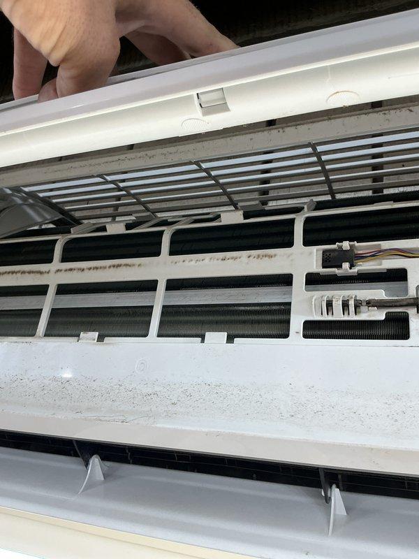 Performed comprehensive clean and check maintenance on wall-mounted mini split system. Removed front cover to access internal components, revealing significant dust and debris accumulation on evaporator coil fins, white plastic housing, and interior surfaces. Thoroughly cleaned evaporator coil assembly, removed buildup from black horizontal fins, and sanitized all accessible interior components. Verified unit specifications and safety labels, including A2L refrigerant classification warnings and electrical shock hazard notices. System restored to optimal operating condition with improved airflow efficiency following complete cleaning procedure.