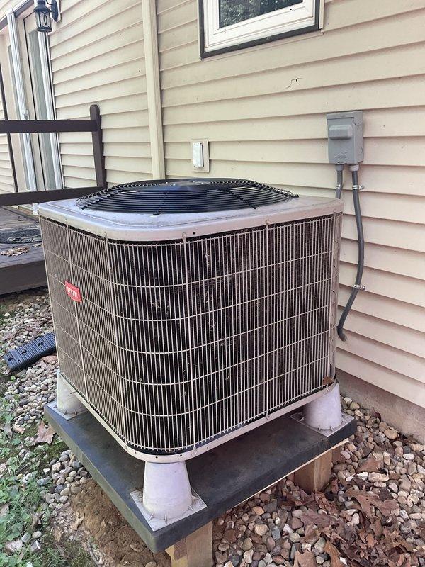 Technician responded to service call to assess existing HVAC system and provide replacement equipment pricing. Upon inspection, documented current Bryant split system consisting of outdoor cylindrical condensing unit mounted on elevated PVC platform with gravel base and indoor vertical air handler unit installed in utility space alongside water heater. System components photographed including electrical disconnect, condensate drainage piping, ductwork connections, and overall installation configuration to develop accurate replacement proposal for homeowner's review.