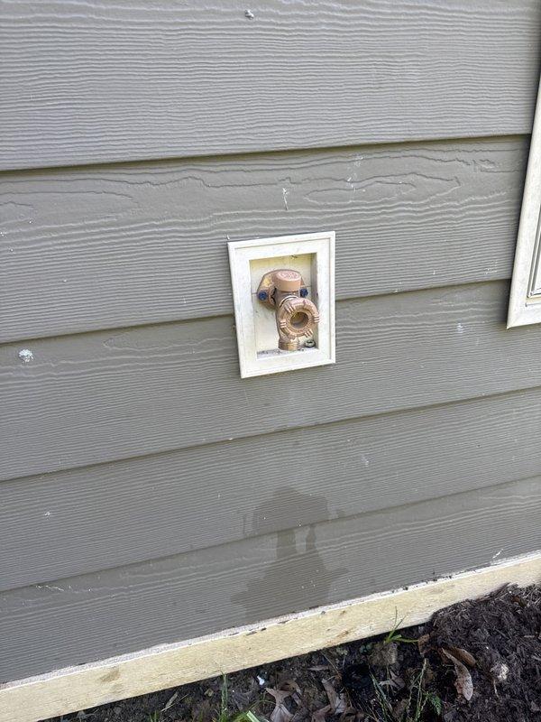 Replaced defective exterior water spigot with new brass hose bib and installed white access panel on gray lap siding for improved maintenance access. Ensured proper mounting to exterior wall above foundation and verified water flow functionality upon completion.