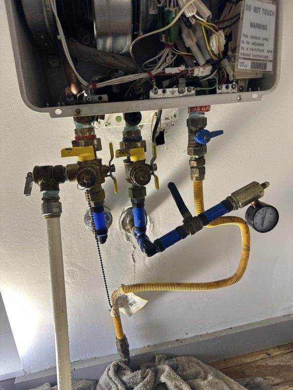 Completed installation of customer-provided tankless water heater unit with LPG gas connection. Mounted unit to wall, connected water supply lines with isolation valves featuring shutoff controls, installed flexible yellow corrugated gas line with proper fittings and pressure gauge, and verified all electrical wiring connections within the unit. Tested system operation including heat exchanger, blower motor assembly, ignition controls, and safety mechanisms to ensure proper functionality. All plumbing connections secured with brass fittings and isolation valves for maintenance access, ventilation ductwork properly connected, and unit confirmed operational.