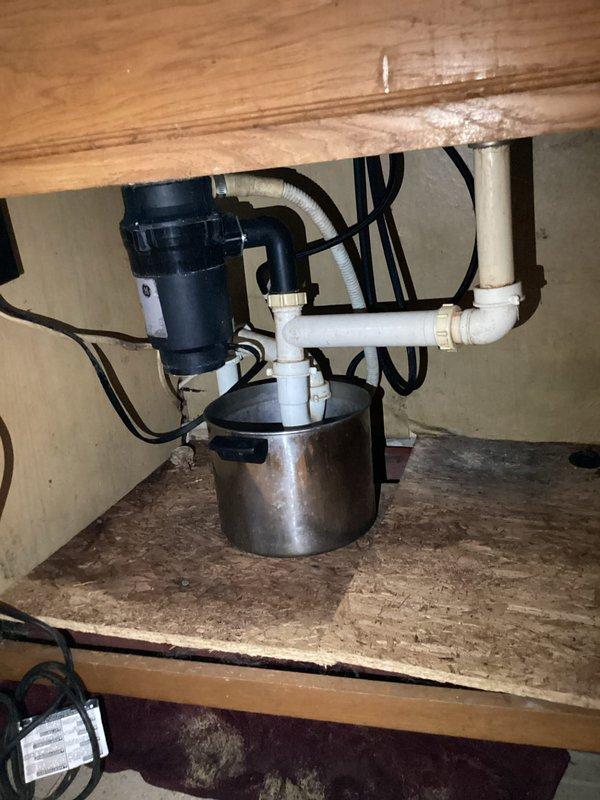 Responded to kitchen drain clog complaint and performed inspection of plumbing system beneath sink. Upon assessment, found garbage disposal unit and PVC drain assembly in working order with no visible blockages in the accessible trap configuration. Identified significant corrosion on copper plumbing components in the drainage system, including advanced oxidation with green patina buildup on copper fittings that may impact long-term system integrity. Cleared drainage issue and verified proper flow restoration through the disposal and drain lines.