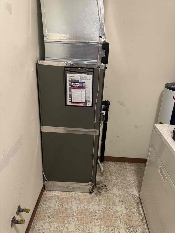 Completed full commercial HVAC system installation in interior utility room, including vertical air handler unit with associated ductwork and refrigerant lines. Rerouted electrical wiring to accommodate new equipment configuration and ensure proper power supply to system components. System installed in corner configuration with supply ductwork extending through ceiling, all connections secured and tested for proper operation.