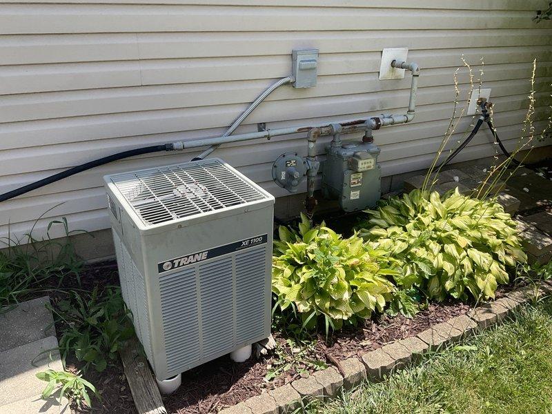 Conducted comprehensive cooling system evaluation on 28-year-old Trane XE 1100 air conditioning unit located on exterior concrete pad. Documented existing equipment condition, installation configuration, and surrounding infrastructure including gas meter proximity and electrical disconnect placement. Provided replacement estimate and recommendations based on system age and current operating status.