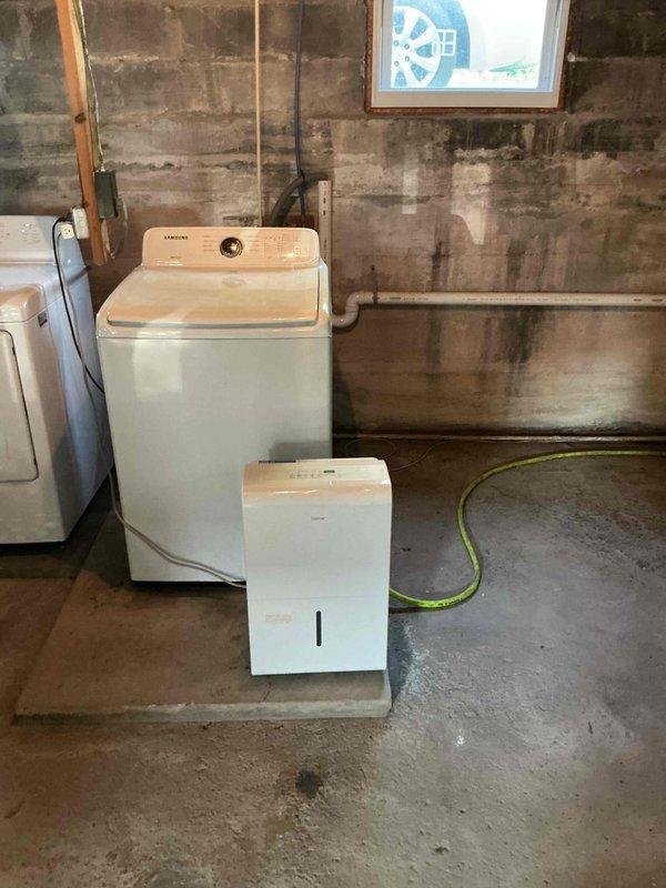 Conducted on-site assessment for basement bathroom and kitchenette installation in unfinished basement space with existing laundry facilities. Documented current conditions including exposed concrete block and brick walls with extensive moisture damage, active water staining, and damp concrete floor requiring remediation prior to fixture installation. Evaluated existing plumbing infrastructure including white PVC drainage system and washing machine connections to determine routing for new bathroom and kitchenette supply and waste lines. Identified need for moisture mitigation, proper waterproofing, and potential foundation sealing before proceeding with fixture installation to ensure code compliance and prevent future water damage to new installations.