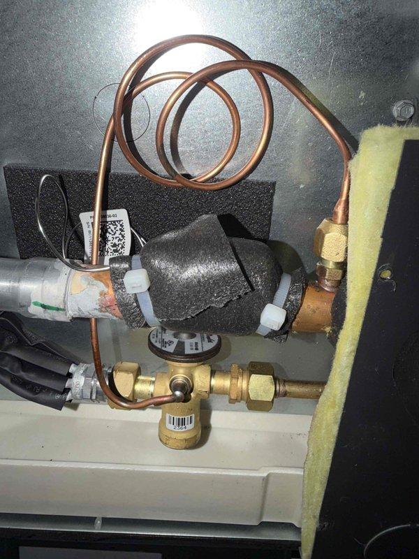 Completed full installation of Lennox heat pump system with associated duct modifications in residential mechanical room. System includes new Lennox air handler unit positioned alongside existing water heater, with copper refrigerant line sets, brass valve assemblies, and insulated flexible ductwork connecting to attic distribution system. All refrigerant connections secured with proper insulation, electrical wiring completed to unit, and system tested for proper operation. Service financing documentation finalized and identification verified on file.