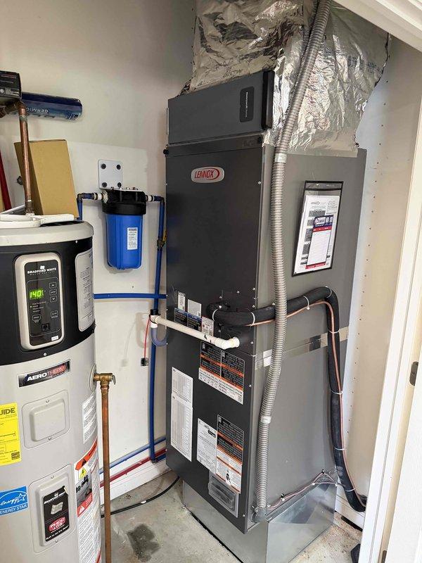 Completed full installation of Lennox heat pump system with associated duct modifications in residential mechanical room. System includes new Lennox air handler unit positioned alongside existing water heater, with copper refrigerant line sets, brass valve assemblies, and insulated flexible ductwork connecting to attic distribution system. All refrigerant connections secured with proper insulation, electrical wiring completed to unit, and system tested for proper operation. Service financing documentation finalized and identification verified on file.