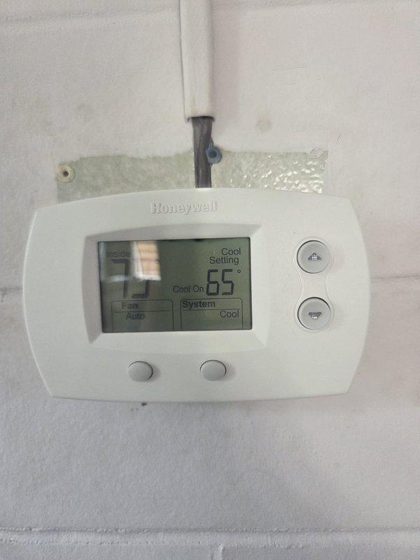 Accessed rooftop unit via interior second-floor hatch and performed A/C service inspection. Verified Honeywell digital thermostat operation showing 65° with system in cooling mode and auto fan setting. Inspected rooftop compressor unit, refrigerant lines, condenser coil, and associated components; noted normal operational wear consistent with equipment age and outdoor exposure.