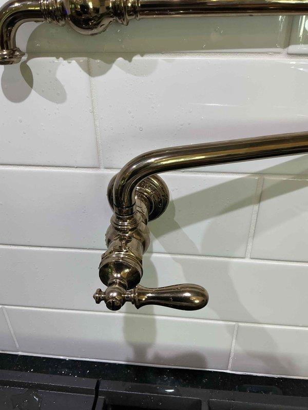 Responded to emergency call for leaking pot filler fixture in commercial facility. Upon arrival, identified active leak at first joint connection from wall valve where spray was occurring during operation. Inspected brass pot filler assembly mounted on subway tile wall, documented condition with photos, and assessed valve connection point requiring repair to restore proper function and prevent water damage.