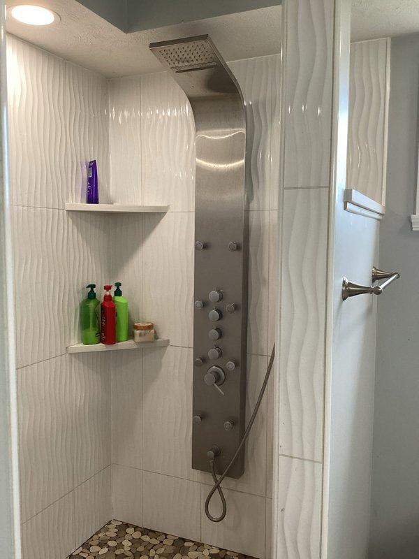Responded to service call for reported leaking in bathtub and shower area. Upon inspection, assessed the shower panel system with multiple control valves and overhead rainfall showerhead configuration. Examined all plumbing connections, fixtures, and water delivery points throughout the tiled shower enclosure. Investigated potential leak sources including the stainless steel shower panel mounting points, control valve assemblies, and drain assembly. Documented existing conditions with photographic evidence for service records. Identified and addressed water intrusion issues to restore proper functionality to the bathing fixtures.