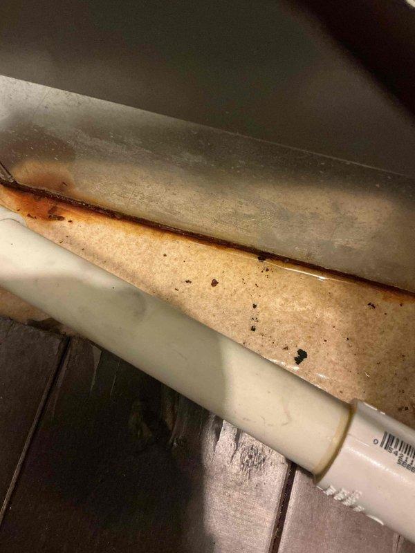 Responded to service call for suspected water softener leak. Upon inspection, discovered the issue was actually related to HVAC condensate drainage system rather than the water softener. Found significant rust staining and corrosion on the evaporator coil drain pan, with visible mineral deposits and debris accumulation indicating chronic moisture exposure. The condensate drain line showed signs of previous drainage issues that had caused water damage to the metal components. Documented conditions with photographs showing the extent of rust damage on the drain pan surfaces and the PVC condensate line configuration for future reference and potential follow-up maintenance recommendations.