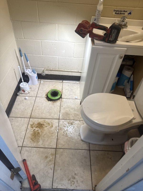 Responded to commercial office bathroom experiencing water seepage through flooring for approximately three weeks. Upon inspection, identified multiple areas of water infiltration causing visible staining and discoloration across tile flooring. Investigated toilet fixture and surrounding plumbing connections for potential leak sources. Assessed floor drain system and verified proper drainage function. Documented existing water damage patterns and active moisture presence throughout bathroom space. Recommended further investigation of subfloor conditions and potential underground plumbing line issues to determine root cause of chronic water intrusion.