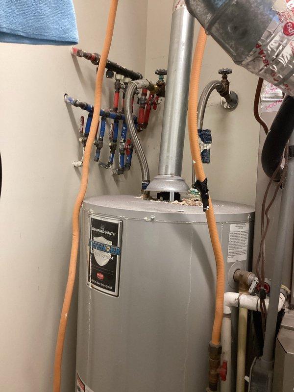 Responded to service call for water heater pilot light repeatedly extinguishing. Upon inspection, discovered debris accumulation on top of tank near flue pipe, which can interfere with proper combustion air flow and draft. Inspected thermocouple, pilot assembly, and gas control valve for proper operation. Verified all plumbing connections, shut-off valves, and supply lines were functioning correctly. Documented existing installation configuration including hot and cold water connections with color-coded ball valves and flexible supply lines. Photographed conditions for service records.