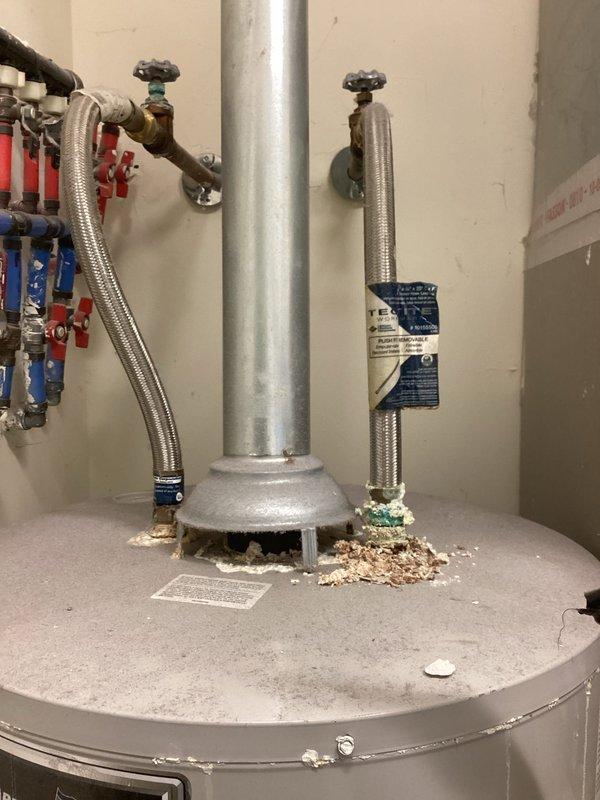 Responded to service call for water heater pilot light repeatedly extinguishing. Upon inspection, discovered debris accumulation on top of tank near flue pipe, which can interfere with proper combustion air flow and draft. Inspected thermocouple, pilot assembly, and gas control valve for proper operation. Verified all plumbing connections, shut-off valves, and supply lines were functioning correctly. Documented existing installation configuration including hot and cold water connections with color-coded ball valves and flexible supply lines. Photographed conditions for service records.