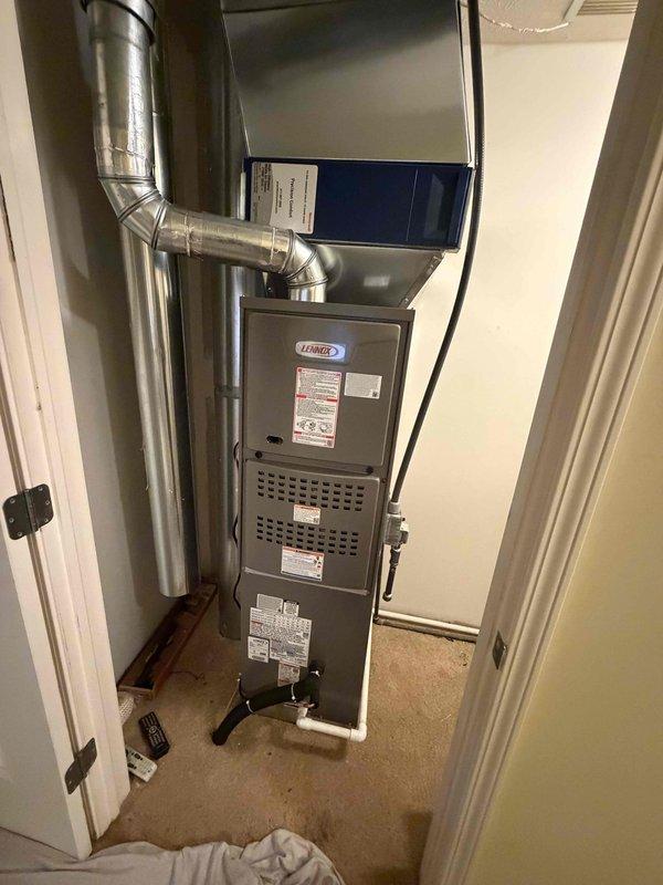 Completed full HVAC system installation consisting of a Lennox air conditioning unit and 80% efficiency gas furnace in residential utility closet. Installed gray Lennox furnace as primary heating unit with proper ventilation grilles and manufacturer specification labels affixed. Mounted blue air handler component above furnace unit and connected metallic supply ductwork with curved elbow joints running vertically along wall. 

Completed all refrigerant line connections using copper piping with brass valve fittings at connection points. Applied black foam pipe insulation to refrigerant lines and secured all piping with cable ties for proper support. Installed yellow foam insulation on additional pipe runs to prevent condensation and maintain system efficiency. Connected flexible ductwork to distribution system and ensured all mechanical components properly secured within confined installation space. Verified all manufacturer labels, safety information plates, and specification tags prop