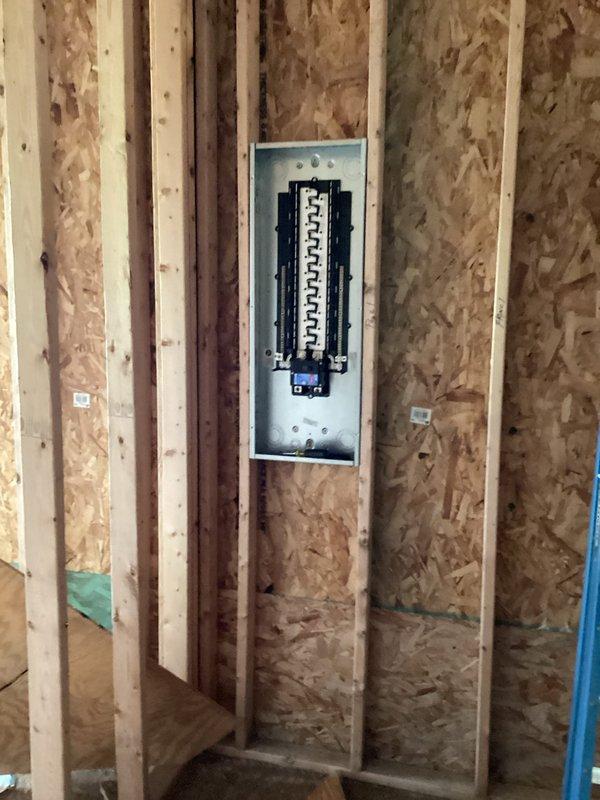 Completed electrical rough-in installation for new construction project, including installation and wiring of main electrical panel with circuit breakers and bus bar configuration. All rough-in work performed to code specifications with panel properly mounted between wall studs during framing phase, ready for insulation and drywall installation.