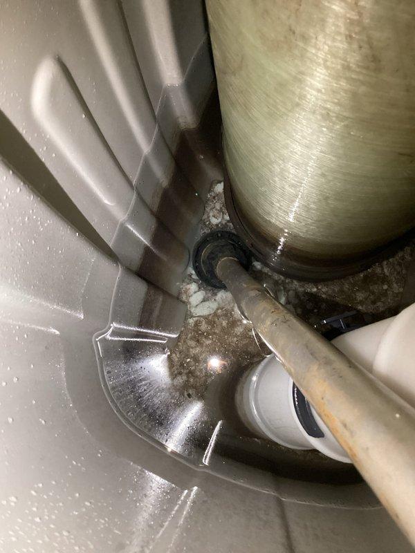 Responded to service call for non-functioning water softener with advance button malfunction and unit filled with water. Inspected water softener system and identified control valve issue preventing proper regeneration cycle. Addressed mechanical failure of advance button mechanism and assessed water level concerns within brine tank. Additionally performed requested water heater flush service, draining sediment buildup from tank bottom to improve heating efficiency and extend equipment lifespan. Documented equipment conditions with photographs showing water heater installation with drain pan, plumbing connections, and disposal unit for service records.