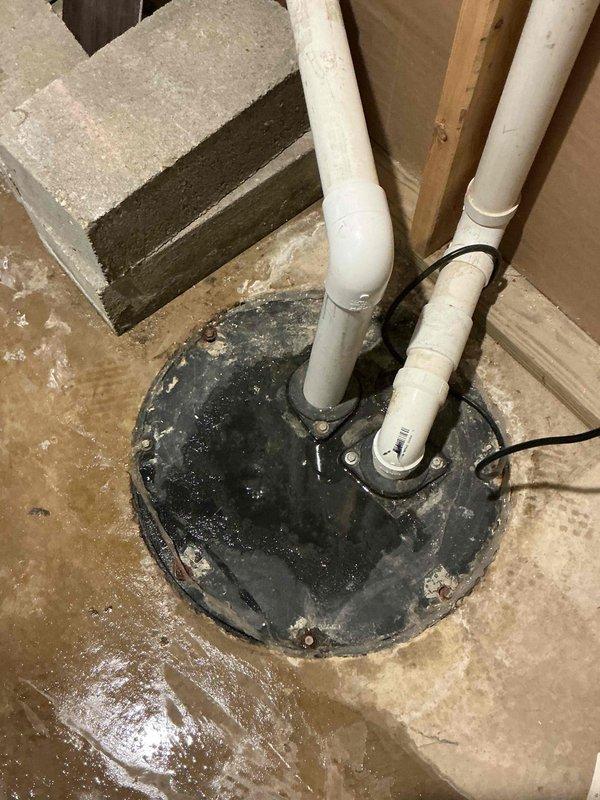 Responded to basement water leakage complaint originating from sump pump system. Upon arrival, inspected sump pump pit and surrounding area, noting significant water staining and moisture patterns on concrete floor indicating recent flooding events. Assessed sump pump installation, discharge piping, and pit cover assembly. Documented existing conditions showing weathered pit cover with mineral deposits, properly secured PVC discharge lines, and evidence of water intrusion around the system. Cleaned up standing water from basement floor and verified sump pump operation and discharge flow. Confirmed water softener was not the source of leakage as initially suspected by homeowner.