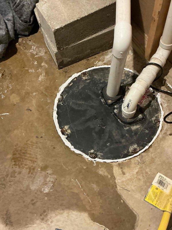 Responded to basement water leakage complaint originating from sump pump system. Upon arrival, inspected sump pump pit and surrounding area, noting significant water staining and moisture patterns on concrete floor indicating recent flooding events. Assessed sump pump installation, discharge piping, and pit cover assembly. Documented existing conditions showing weathered pit cover with mineral deposits, properly secured PVC discharge lines, and evidence of water intrusion around the system. Cleaned up standing water from basement floor and verified sump pump operation and discharge flow. Confirmed water softener was not the source of leakage as initially suspected by homeowner.