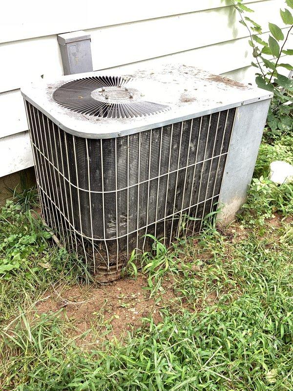 Responded to service call for rattling noise from AC unit, which customer had turned off prior to arrival. Upon inspection, found outdoor condenser unit showing significant weathering and age-related deterioration, with visible rust staining on top panel and debris accumulation around cabinet. Documented unit condition with photographs showing electrical wiring connections behind protective grating and overall exterior condition of condenser. Unit remains offline pending further diagnostic work or repair approval.