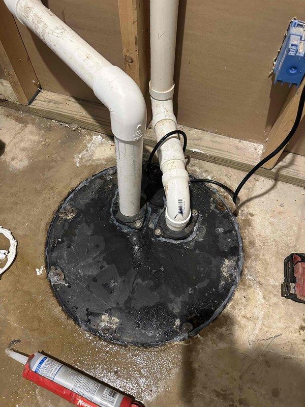 Responded to ongoing water intrusion issue in basement utility area related to sump pump system malfunction. Upon arrival, found standing water covering concrete floor throughout the space, with visible pooling and water damage extending across multiple areas. Inspected sump pump basin and discharge piping configuration, which included dual PVC vertical discharge lines with visible residue buildup. Documented existing conditions showing active water leakage on floor surfaces, indicating pump failure or discharge line compromise. This represents a follow-up visit to address recurring water management system failure requiring further diagnostic evaluation and repair.