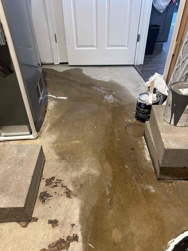 Responded to ongoing water intrusion issue in basement utility area related to sump pump system malfunction. Upon arrival, found standing water covering concrete floor throughout the space, with visible pooling and water damage extending across multiple areas. Inspected sump pump basin and discharge piping configuration, which included dual PVC vertical discharge lines with visible residue buildup. Documented existing conditions showing active water leakage on floor surfaces, indicating pump failure or discharge line compromise. This represents a follow-up visit to address recurring water management system failure requiring further diagnostic evaluation and repair.