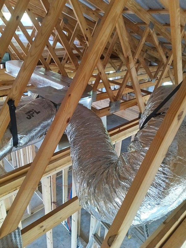 Completed 2-day commercial HVAC rough-in installation for new construction project, including installation of flexible ductwork throughout attic space with proper routing through roof truss system. All ductwork secured to framing members and insulation materials staged for final installation phase.