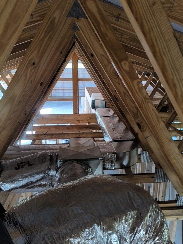 Completed 2-day commercial HVAC rough-in installation for new construction project, including installation of flexible ductwork throughout attic space with proper routing through roof truss system. All ductwork secured to framing members and insulation materials staged for final installation phase.