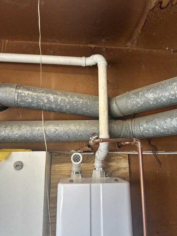 Completed installation of tankless water heater in basement utility area, including all necessary gas line connections with shut-off valve, copper supply piping with PVC vent connections, and pressure relief valve. Unit was mounted securely to wooden wall surface and all plumbing connections were tested for proper operation and leak-free performance.