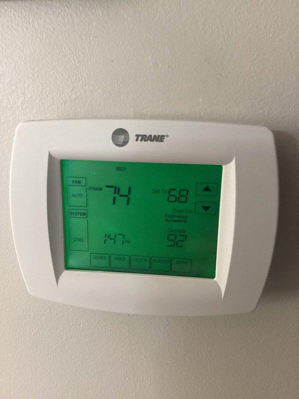 Returned to property to address cooling issue with indoor temperature reading 75°F when thermostat set to 68°F. Inspected Trane programmable thermostat showing current temp 74°F with setpoint at 68°F, indicating system struggling to reach desired temperature. Examined outdoor condensing unit and associated components including refrigerant lines and pump assembly. Equipment showed significant weathering and age-related wear. Documented system conditions with photos for further assessment. Customer had time constraint due to 2 PM meeting, so focused on identifying any immediate adjustments possible to improve short-term cooling performance while system operates.