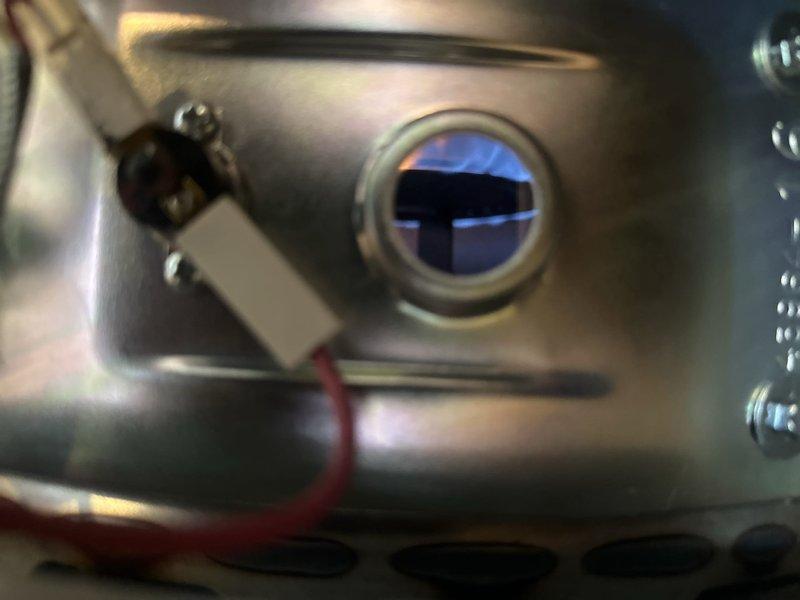 Performed inspection and maintenance on tanked water heater combustion system. Verified proper ignition and flame operation through viewing port, confirming healthy blue flame pattern indicating complete combustion. Inspected flame sensor electrode and associated wiring connections for secure mounting and proper electrical continuity. All combustion components operating within normal parameters and unit functioning safely.