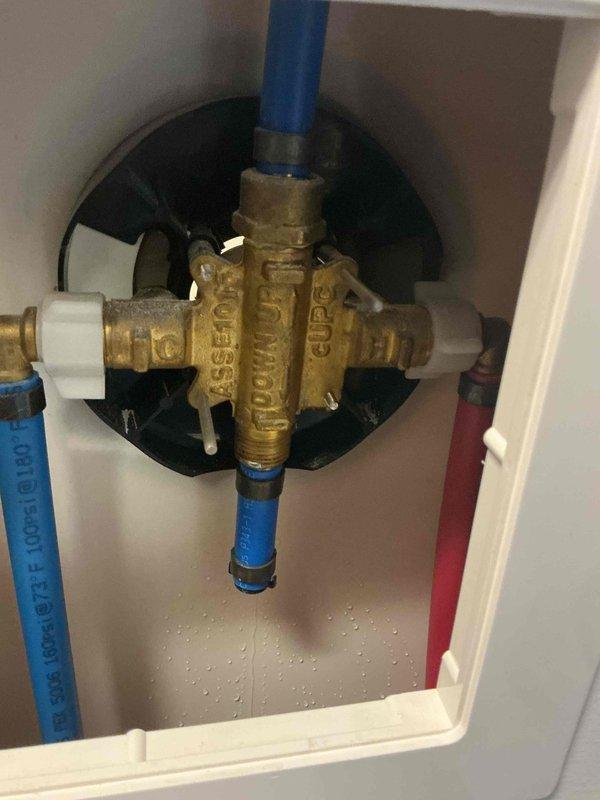 Responded to complaint of low water pressure in shower that had persisted for an extended period. Upon inspection, accessed the shower valve assembly through the utility panel and examined the brass mixing valve, PEX supply lines, and associated connections. Documented the shower control fixture showing mineral deposits and water staining around the escutcheon plate, indicating potential internal valve deterioration affecting flow rate. Photographed the plumbing assembly including the brass manifold valve with blue PEX connections and mounting components to document current system configuration for recommended repairs or valve replacement to restore proper water pressure.