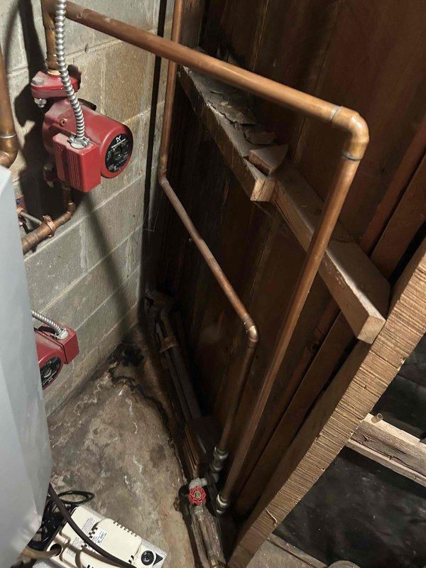 Performed comprehensive boiler maintenance and inspected hydronic heating system for reported leak. Thoroughly examined dual circulator pump assembly, copper piping loop configuration, and all soldered joints throughout the system. Identified moisture concerns in mechanical room with visible floor staining and efflorescence on concrete surface, inspected all pipe connections, valve assemblies, and flexible connectors for signs of active leakage. Documented condition of circulator pumps with control dials, bypass piping arrangement, and shut-off valves. Assessed aged plumbing installation including copper pipe oxidation patterns and all fittings in utility space. System operational at time of inspection; recommended monitoring for active leak source and potential follow-up for identified moisture issues.