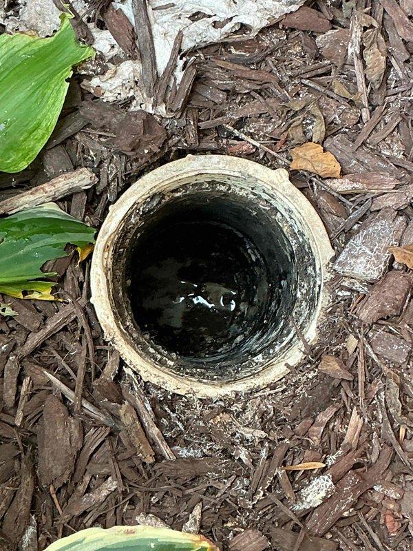 Responded to clogged drain line located in patio area near AC unit. Upon arrival, inspected cleanout access point embedded in landscaped mulch bed. Line had been previously snaked multiple times without resolution. Performed camera inspection of drain line to identify blockage location and cause. Documented cleanout condition showing signs of moisture and standing water within pipe. Additionally inspected exterior hose bibb with broken handle as requested. Photographed cleanout access and surrounding area for service documentation.