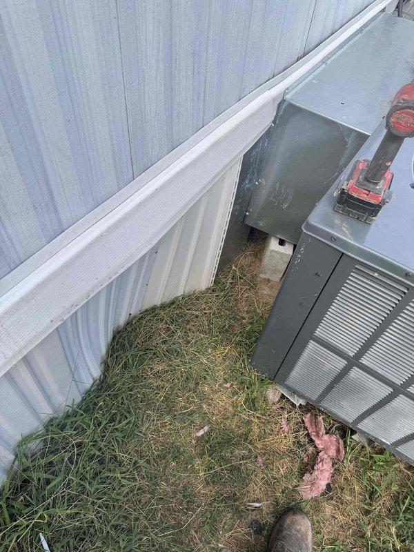 Completed installation of outdoor HVAC condensing unit positioned against corrugated metal exterior wall with proper electrical disconnect box and conduit connections. Modified return air ductwork to proper sizing per specifications and installed refrigerant line set with appropriate valve configuration. Unit was positioned in narrow service corridor with adequate clearance for maintenance access, all electrical connections secured, and system verified operational.