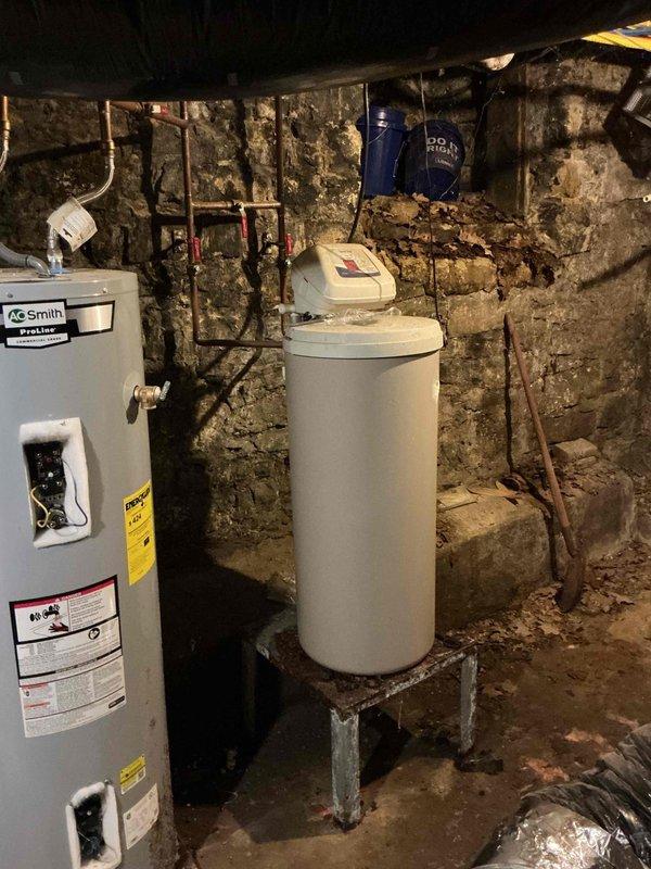 Responded to no hot water complaint at residential property. Upon inspection of basement utility area, evaluated AO Smith water heater and associated plumbing system. Documented existing conditions of water heater, surrounding copper piping, electrical connections, and control panels. Photographed installation configuration including water softener system, expansion tank, and stone wall plumbing layout for service records.
