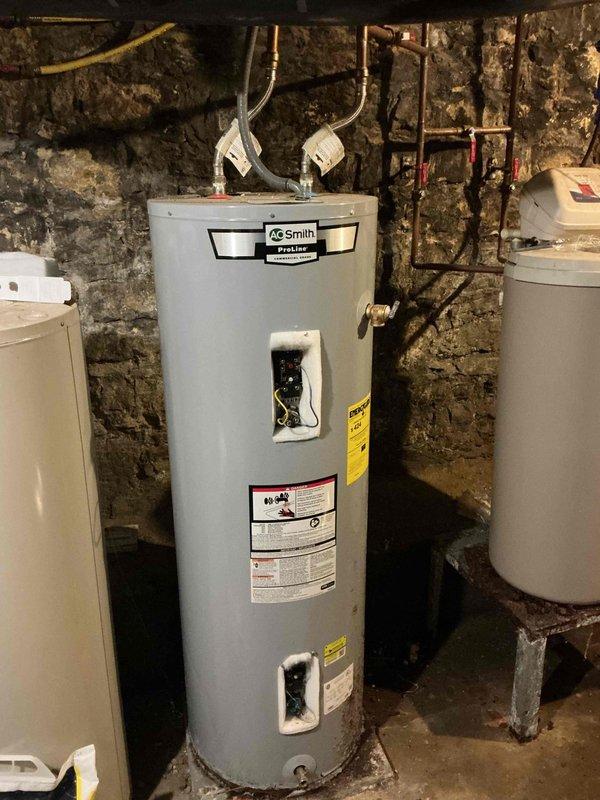 Responded to no hot water complaint at residential property. Upon inspection of basement utility area, evaluated AO Smith water heater and associated plumbing system. Documented existing conditions of water heater, surrounding copper piping, electrical connections, and control panels. Photographed installation configuration including water softener system, expansion tank, and stone wall plumbing layout for service records.
